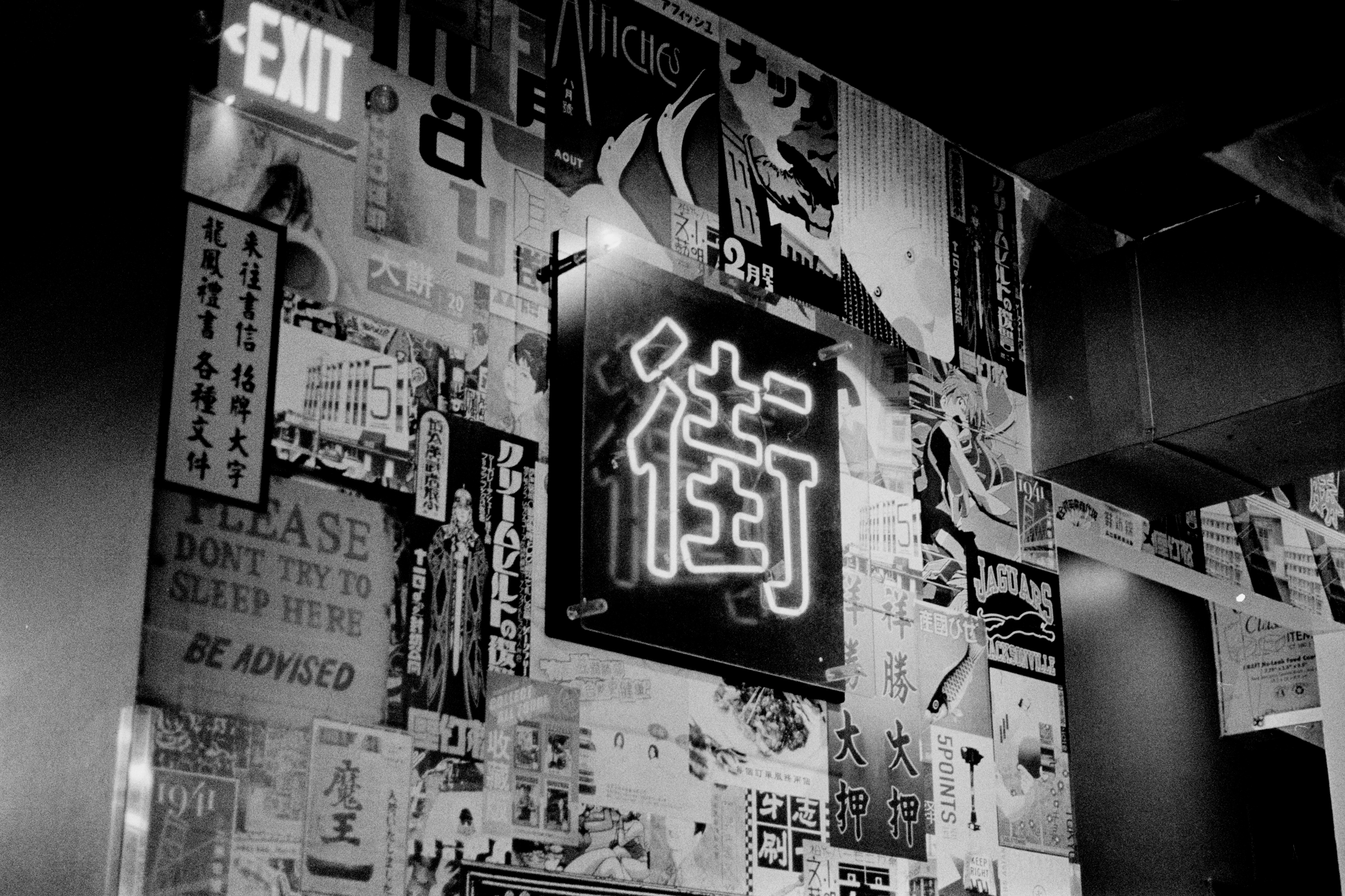 Neon sign of the Kanji 街 (street) on a wall with Japanese posters